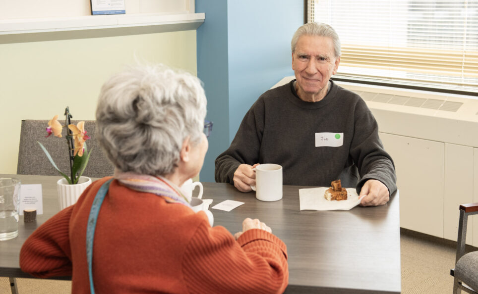 Two older adults impacted by dementia sharing a cup of coffee