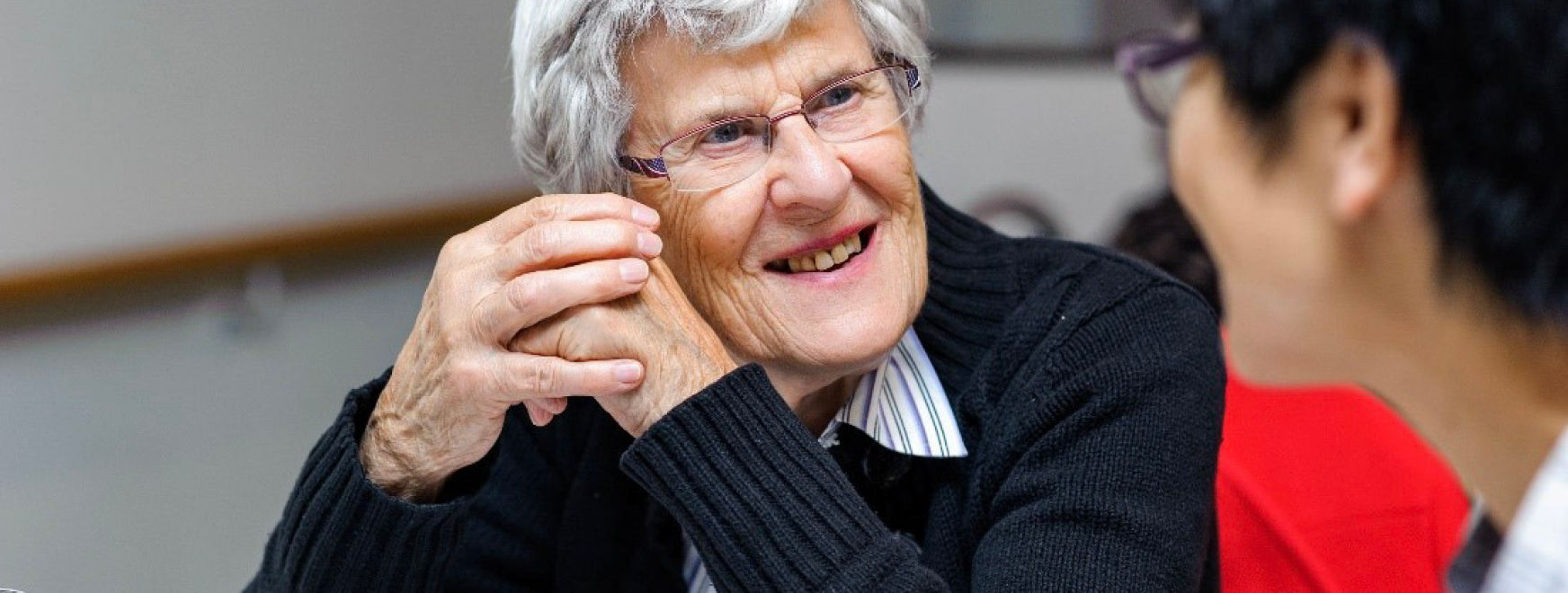 An elderly woman speaking to another person and smiling.