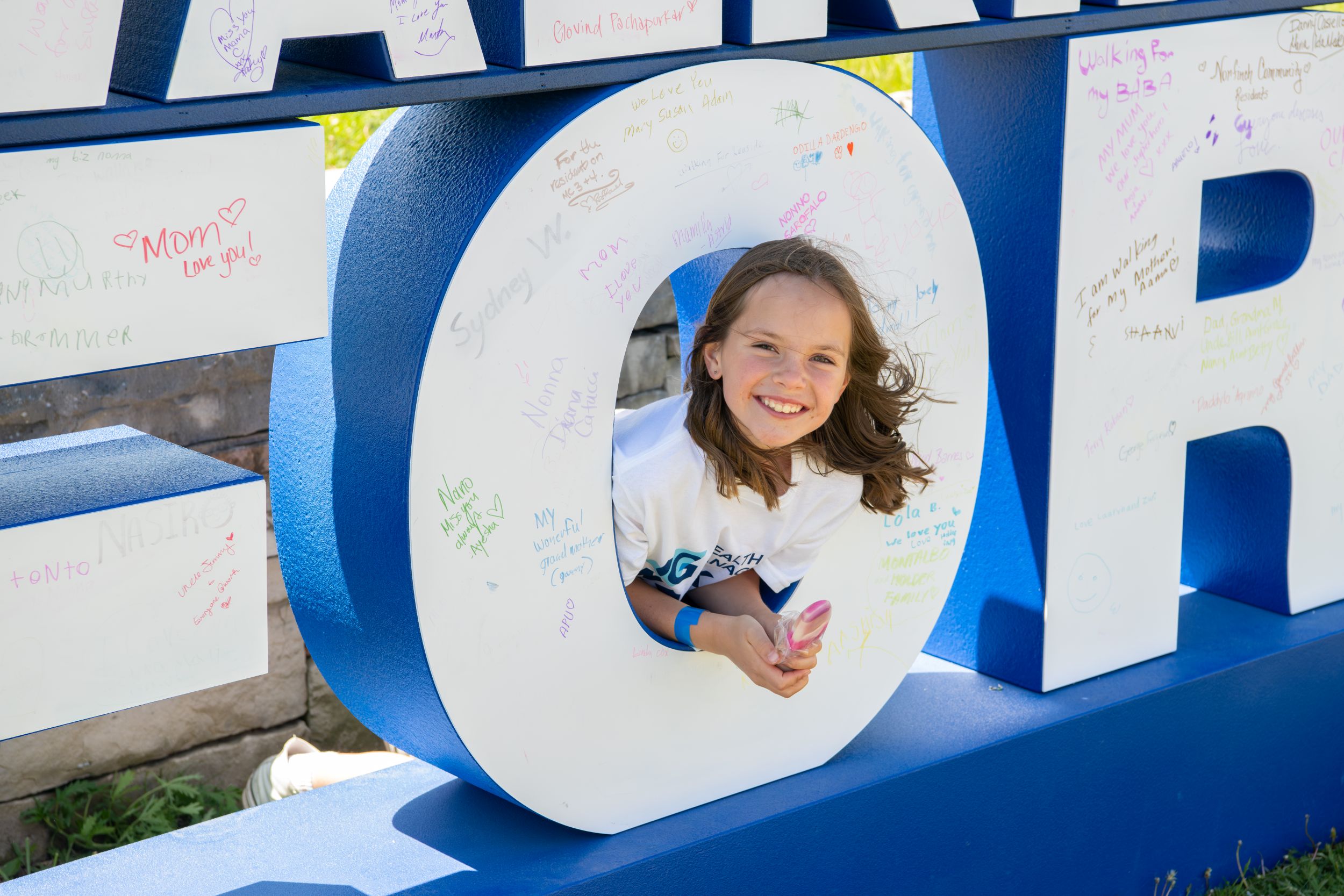 An image of a child posing in the middle of the "O" in the IG Wealth Management Walk for Alzheimer's sign installation.